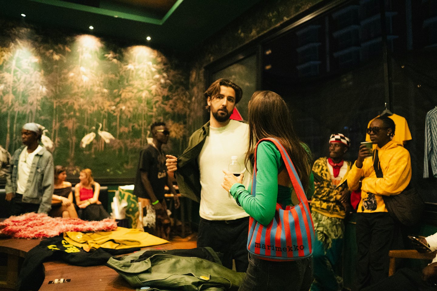 People socialize at a pop-up shop featuring a nature mural.