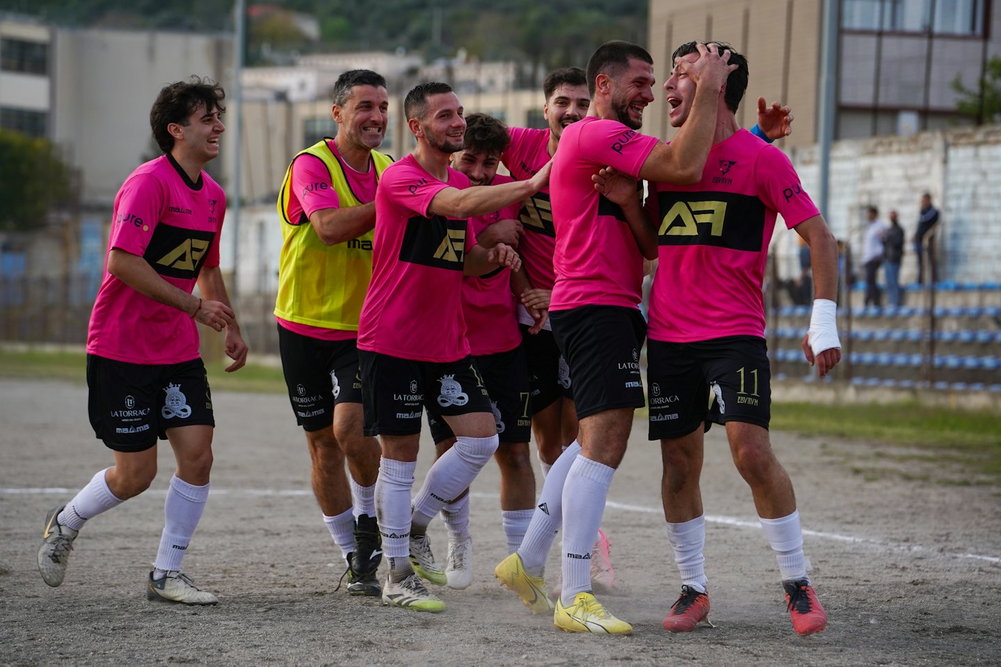 Soccer players in pink and black uniforms celebrate on a field.