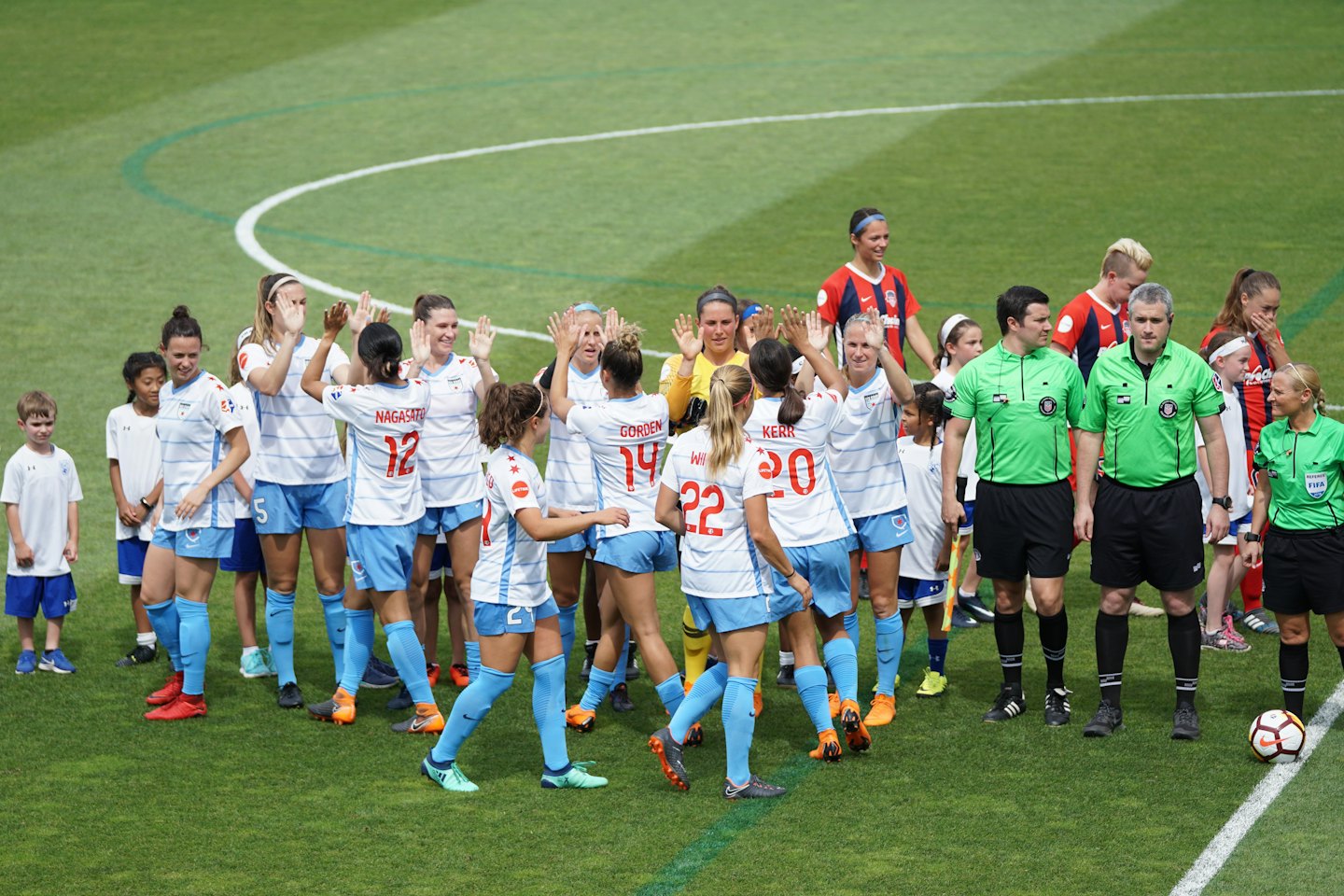 Female soccer players high-fiving on a green field.