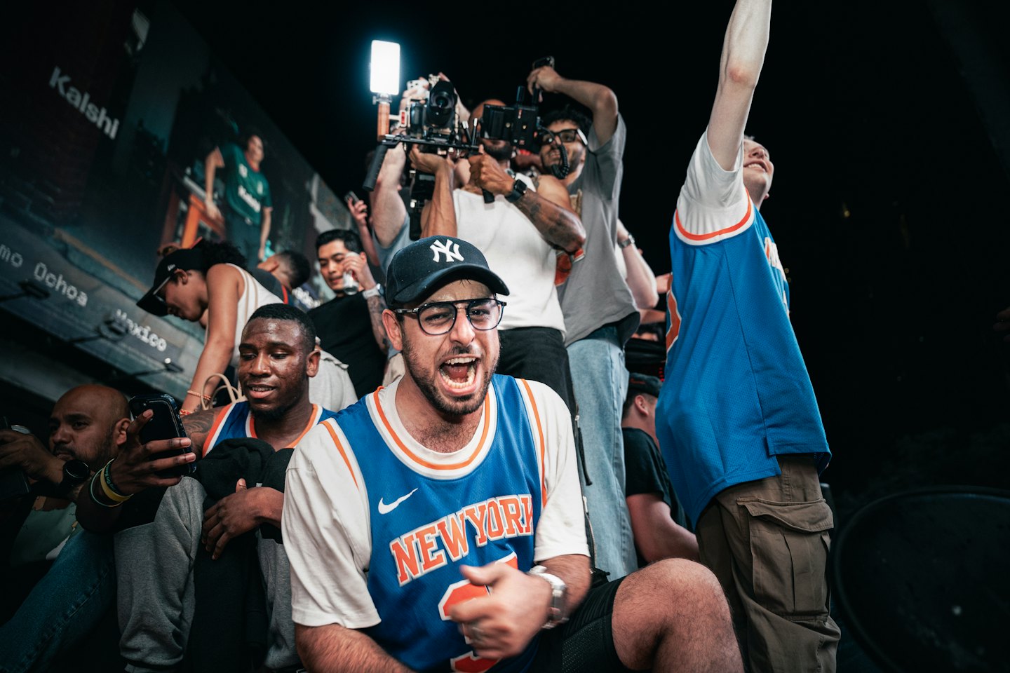 Basketball fans cheering while watching a digital screen outdoors.